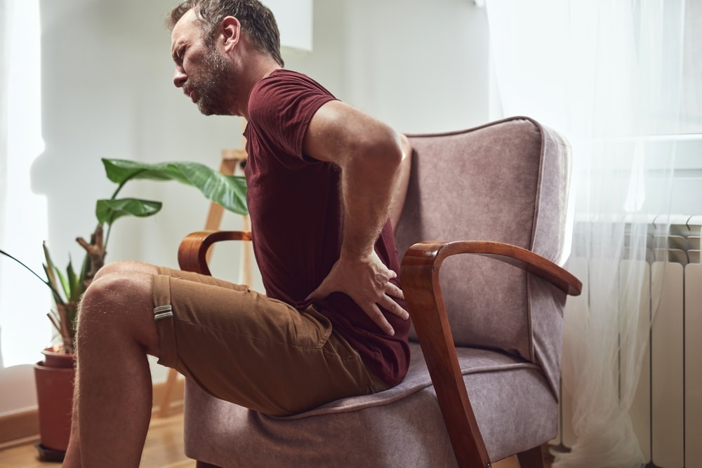 Man sitting down, clutching his hip in pain